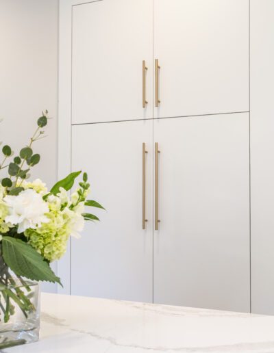 A white kitchen with white cabinets and a vase of flowers.