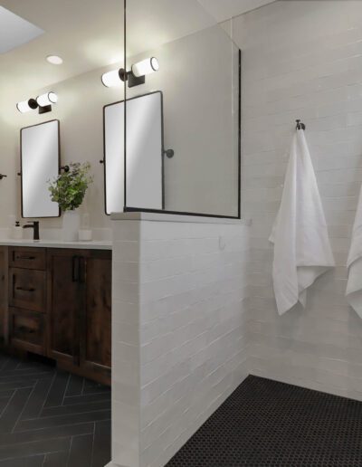 Modern bathroom with white subway tiles, dark wood vanity, two hanging white towels, and black-framed mirrors, illuminated by overhead lights.