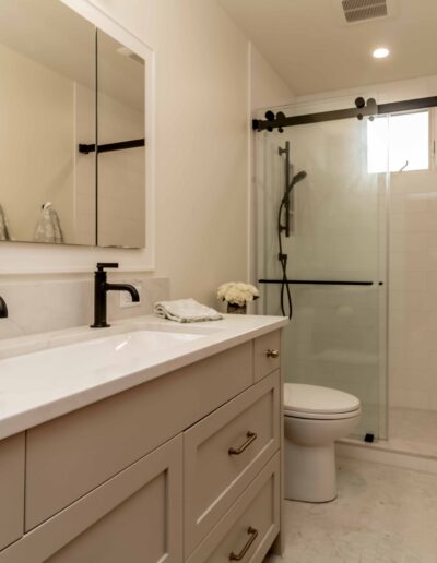 Modern bathroom with a double-sink vanity, black fixtures, a glass-enclosed shower, toilet, and neatly folded towels on the wall.