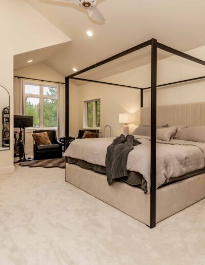 A spacious bedroom with a canopy bed, nightstands, a mirror, exercise equipment by the window, and neutral-colored decor.